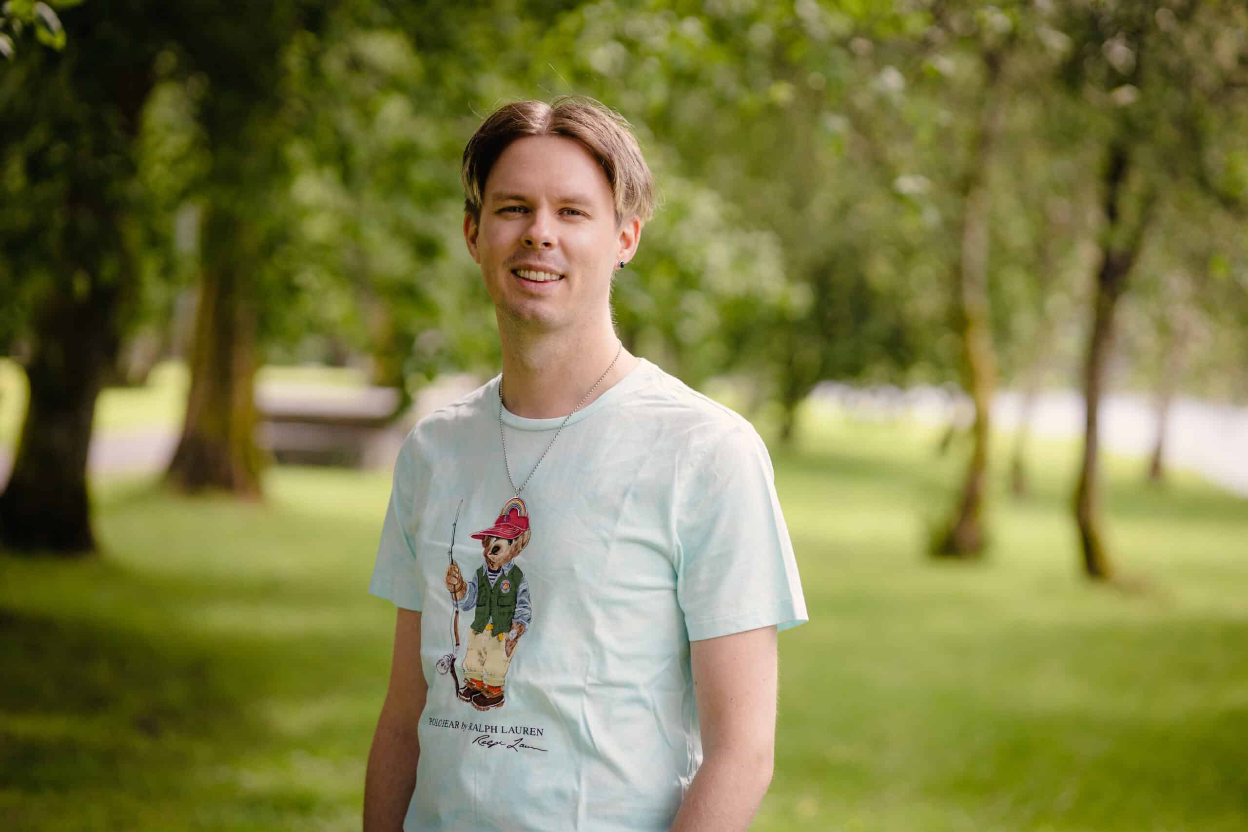 Portrettbilde av H&aring;vard Solbakken, ung mann, ute i en gr&oslash;nn park.